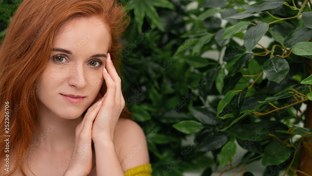 Young redhead woman touching her face, green background Young redhead woman touching her face, green background