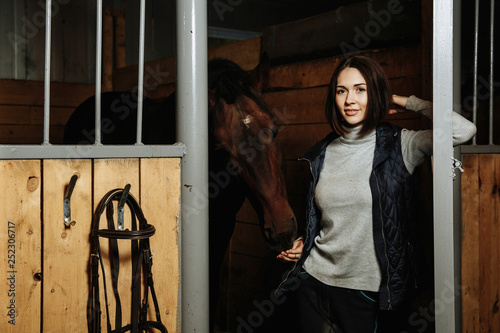 Portrait of smiling female jockey standing by horse in stable