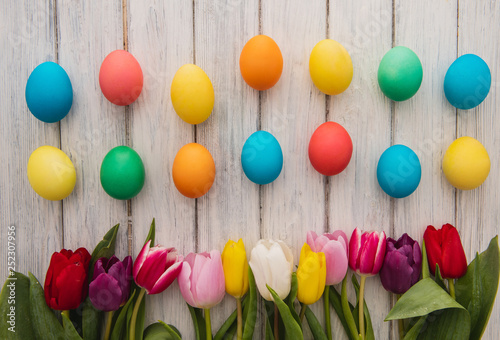 Colorful easter eggs,spring tulips  on wooden texture background.On a white wood table,colored eggs,colors flowers.Happy religious day,traditional for people. Top view.Copy space. © mykola