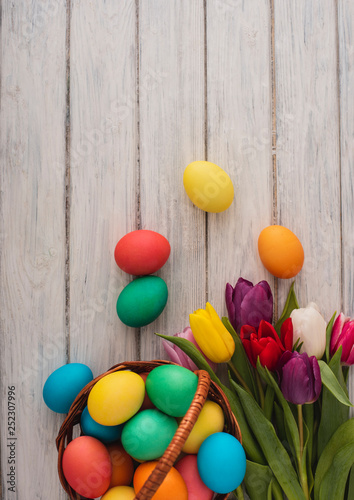Colorful easter eggs spring tulips  on wooden texture background.On a white wood table colored eggs colors flowers.Happy religious day traditional for people. Top view.Copy space.