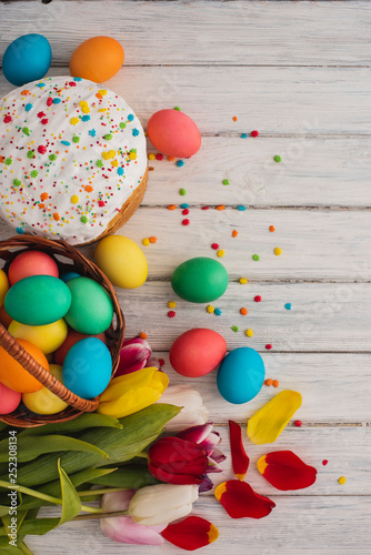 Colorful easter eggs,cake,spring tulips on wooden texture background.On a white wood table,colored eggs,flowers,bread.Happy religious day,traditional for people. Top view.Copy space.