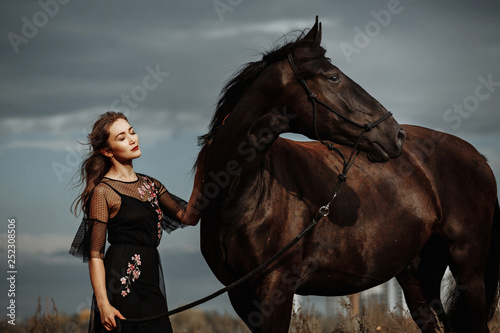 pretty woman with black horse in autumnal nature. Fashion photoshoot