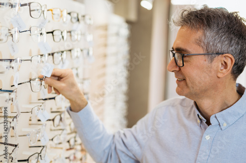middle aged gray haired man choosing eyeglasses in optic store.