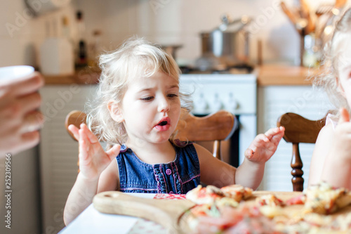 Funny child are eating and tasting italian homemade pizza in cozy home kitchen. Kid is surprised of favorite food. Cute little girl with real  candid emotions. Lifestyle  everyday and authentic moment