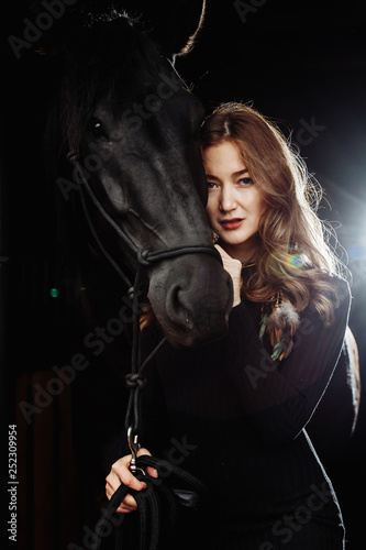 Portrait of young pretty woman and black horse on black background isolated. Fashion concept