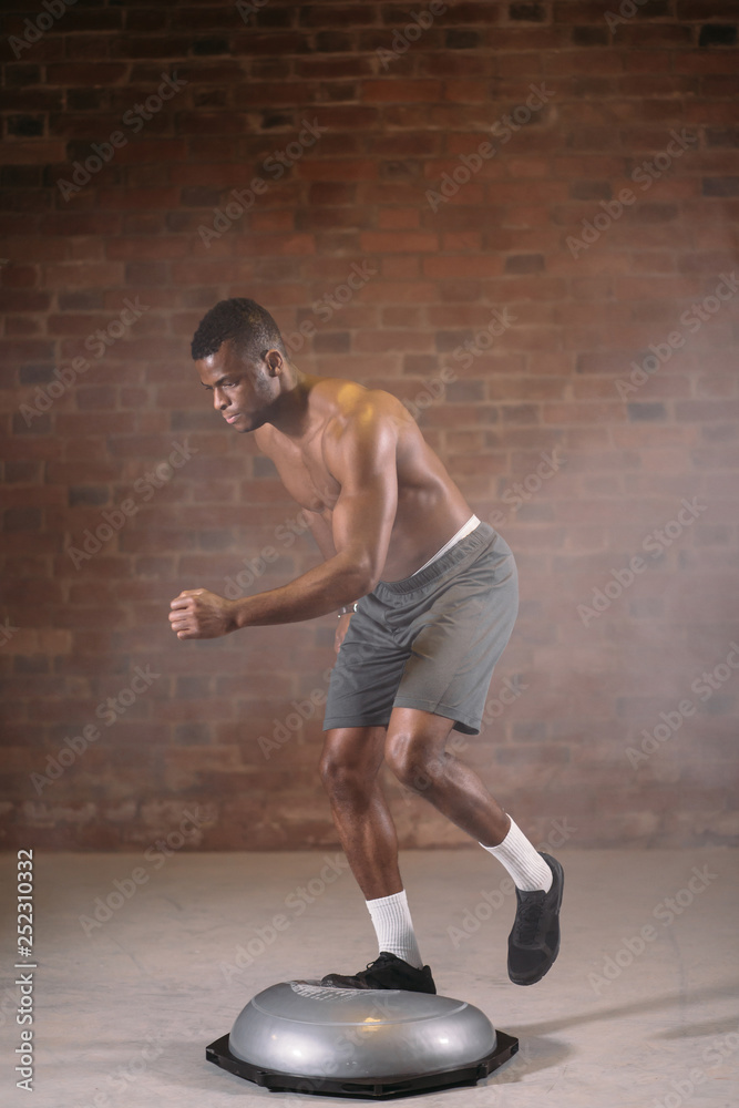 African shortless sportsman performing exercise on bosu ball in crossfit workout gym African shortless sportsman performing exercise on bosu ball in crossfit workout gym