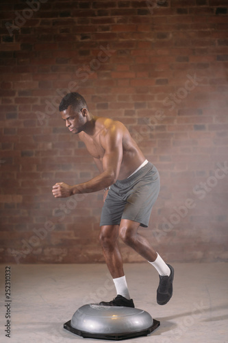 African shortless sportsman performing exercise on bosu ball in crossfit workout gym