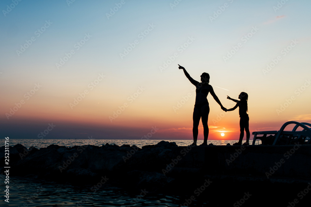 Fototapeta premium Mom and daughter spend time at the sea in the background of the sunset