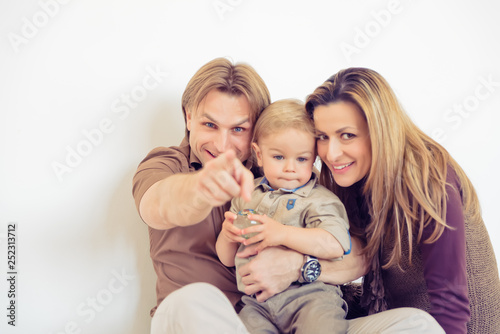 Portrait of happy family sitting on the floor and smiling. Finger pointing.