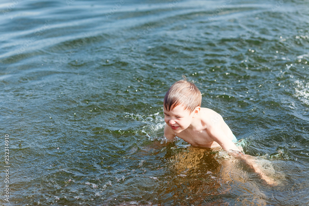 Joyful boy swimming in the lake and splashing in the water. Boy play in water in summer. Joyful boy swimming in the lake and splashing in the water. Boy play in water in summer.