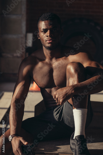 Strong afroamerican athletic man with naked perfect shape muscular body looking at camera isolated over brick background.