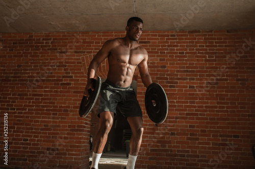 Athletic dark-skinned fitness coach working out with crossfit jumps on giant tire with weighting, therefore training the heart, legs, abdominal muscles and overall endurance.
