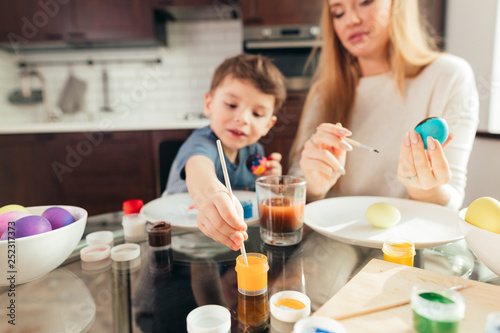 Blonde Female babysitter having confidence  skill and understanding to support children s play  interacting with boy in a playful way  painting eggs to Easter celebration.