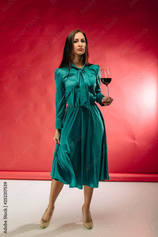 Attractive joyful female model in a green dress and wine glass in hand dancing with pleasure. Adorable caucasian girl at festive and tasting red wine.