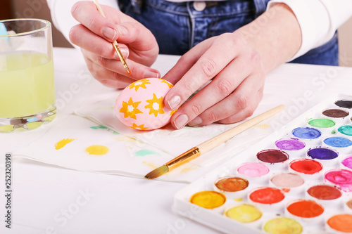 Hand painted Easter eggs, paints and brushes on a white table. Preparation for the holiday. Girls hands draw a pattern.