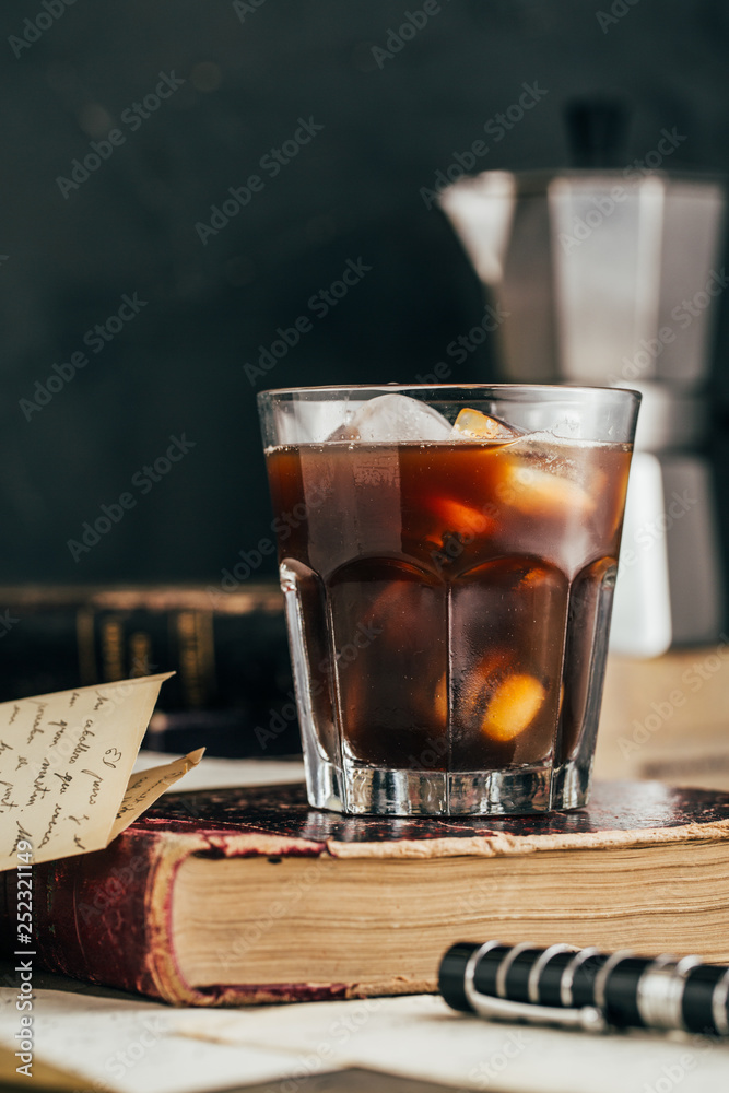 Cold espresso coffee glass in dark grunge mood with antique book Cold espresso coffee glass in dark grunge mood with antique book
