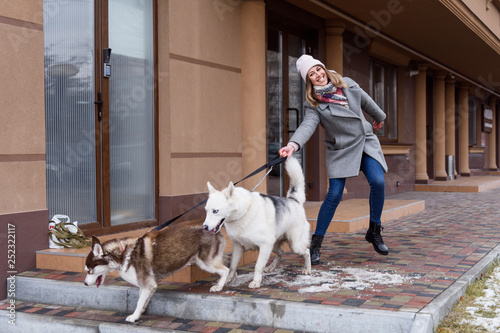 Photography Woman having troubles holding two excited husky dogs on a leash