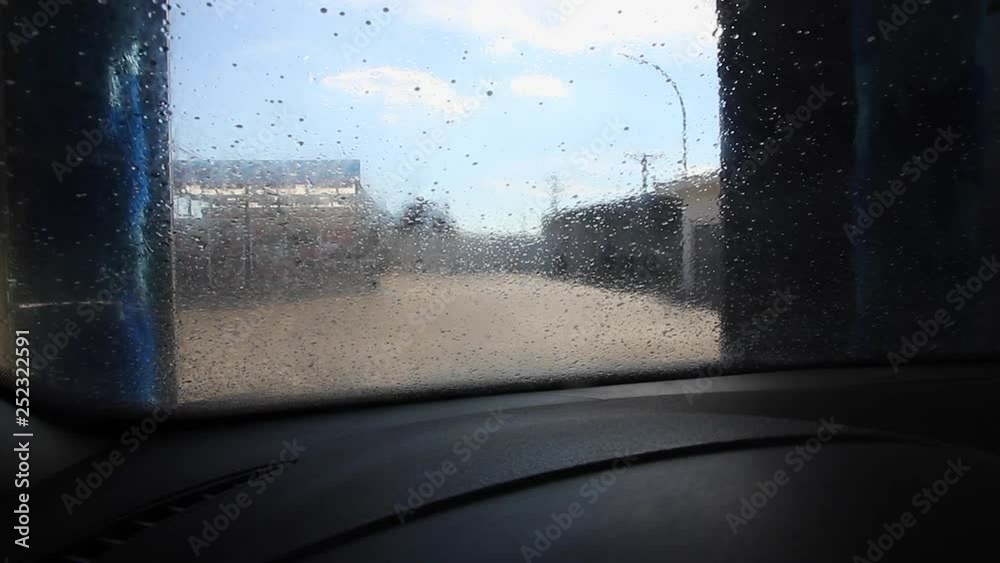 Puente de lavado de coches automatico en el proceso de rociar con agua y espuma de jabón. Comenzando a girar los rodillos sobre el parabrisas. Visto desde el interior del automovil 