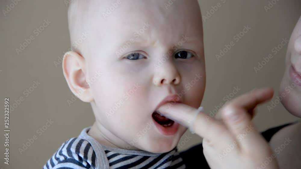 Mom brushes baby's teeth with a silicone brush that fits on her finger Mom brushes baby's teeth with a silicone brush that fits on her finger
