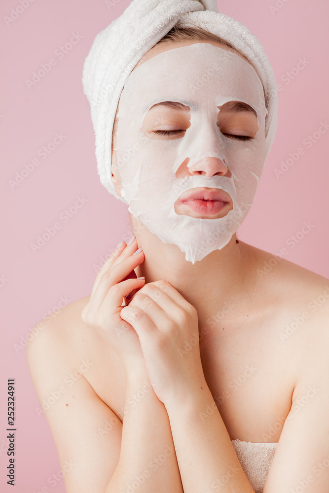 Beautiful young woman is applying a cosmetic tissue mask on a face on a pink background. Healthcare and beauty treatment and technology concept Beautiful young woman is applying a cosmetic tissue mask on a face on a pink background. Healthcare and beauty treatment and technology concept
