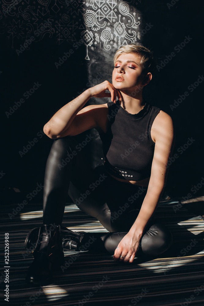 Fashionable gorgeous model in black interior and dark clothes sitting on a floor. Beauty, model concept