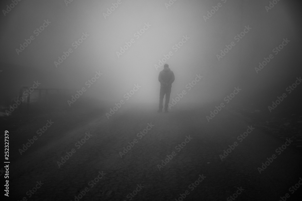 Man walking away on misty road. Man standing alone on rural foggy and misty asphalt road. Man walking away on misty road. Man standing alone on rural foggy and misty asphalt road.