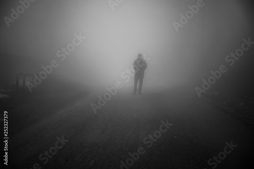 Man walking away on misty road. Man standing alone on rural foggy and misty asphalt road.
