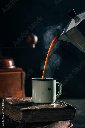 Poring hot coffee in an enamel cup with steam on dark mood
