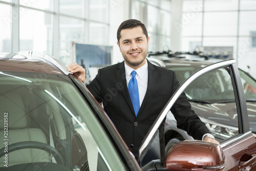 Handsome young businessman choosing a new car at the dealership salon
