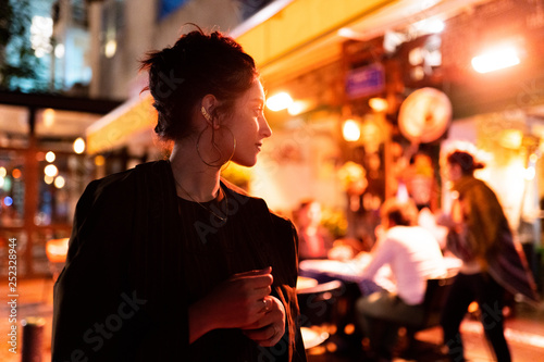 Trendy young hipster with earrings looking away near street cafe at night in Tel Aviv, Israel photo