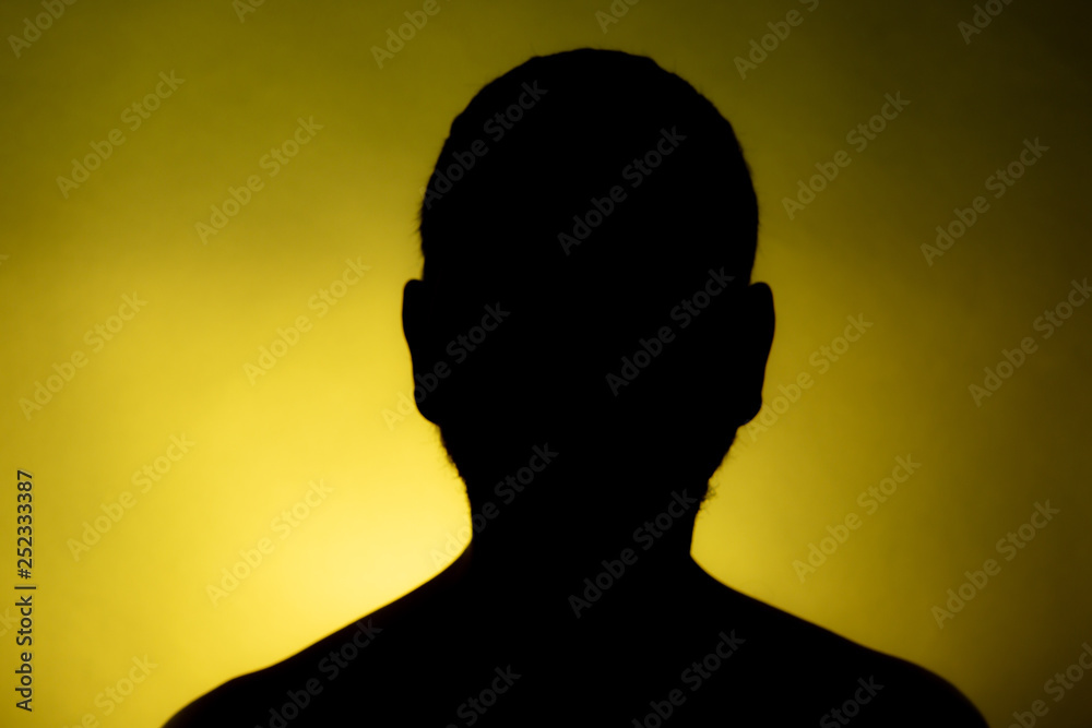 Cleanly defined frontal silhouette of a male person against a blue  background with a spotlight and bright area right behind the bust. Studio  shot with well defined explicit colour background. Stock Photo
