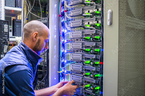  A man works with telecommunications. The technician switches the Internet cable of the powerful routers. A specialist connects the wires in the server room of the data center. photo