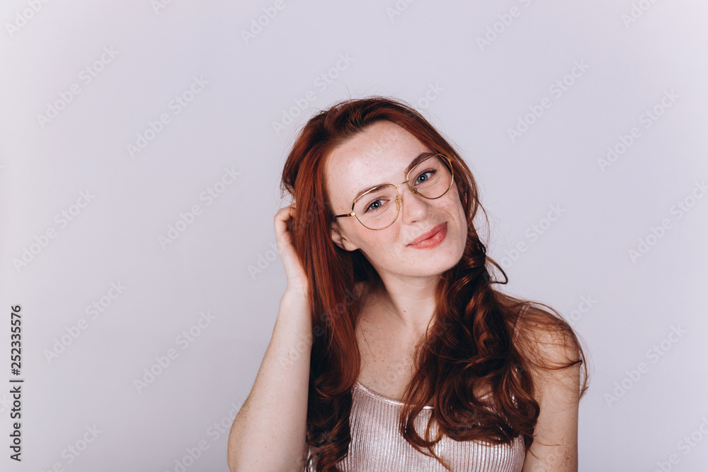 Close up portrait of young ginger pretty emotional caucasian girl with freckles posing in studio on grey background. Beauty, casual, fashion concept
