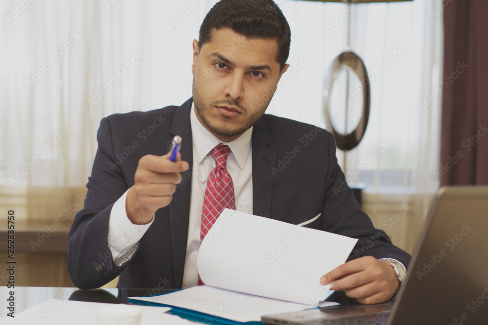 Handsome businessman doing some paperwork and using his laptop Handsome businessman doing some paperwork and using his laptop