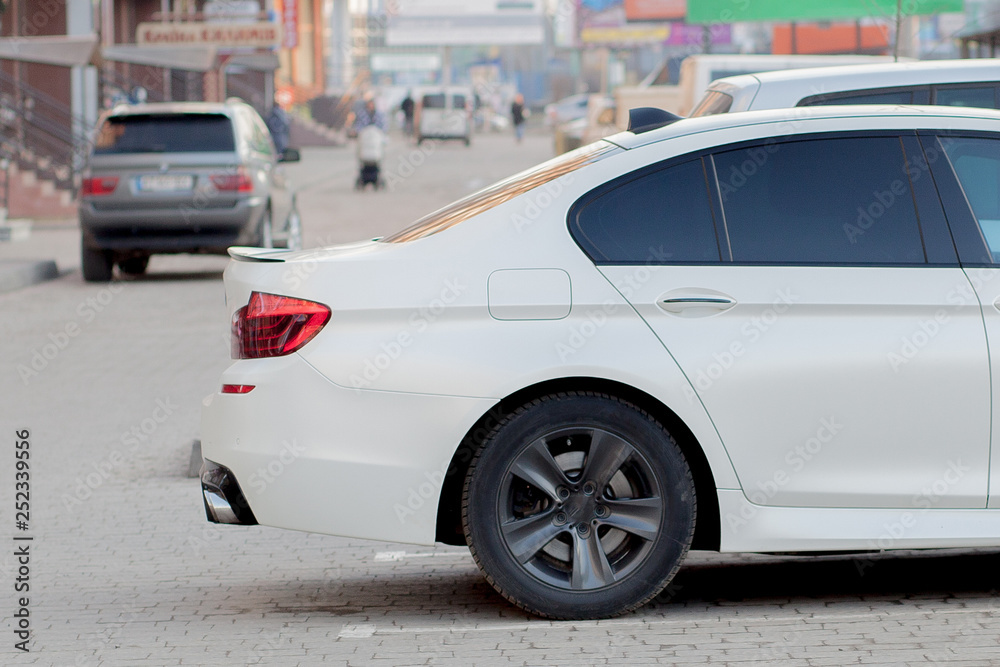 Side view of white car parked in paved parking lot area on blurred suburb road background on bright sunny day. Transportation and parking concept