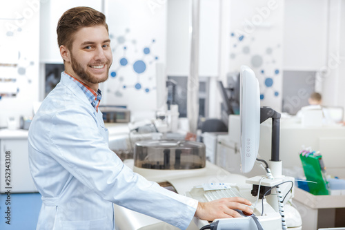 Handsome young male laboratory technician operating computerized analyzing machine