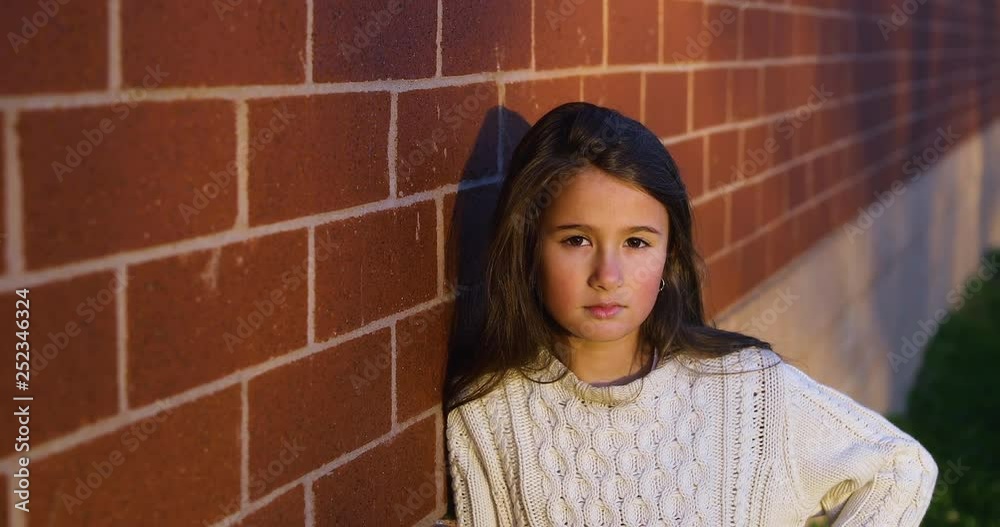 Beautiful portrait of a serious young girl looking at camera during a sunset leaning against a red brick wall. Slow motion 4k. Beautiful portrait of a serious young girl looking at camera during a sunset leaning against a red brick wall. Slow motion 4k.