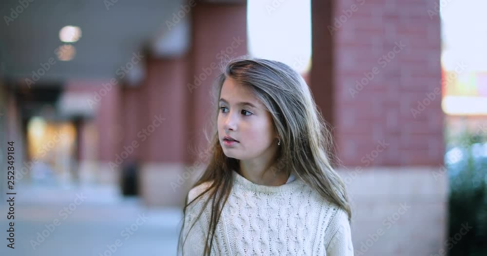 Slow motion of a little, beautiful girl with brownish blonde, long hair and white sweater is lost and wondering around the parking lot of a mall where there are red brick columns behind her. 4k Slow motion of a little, beautiful girl with brownish blonde, long hair and white sweater is lost and wondering around the parking lot of a mall where there are red brick columns behind her. 4k