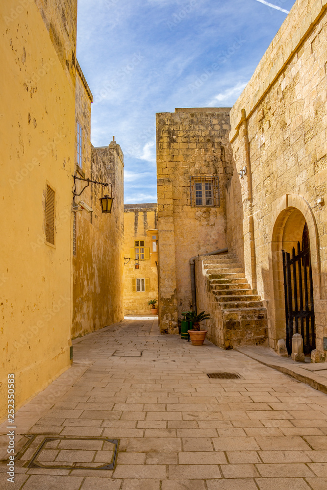 Sunny midday beautiful narrow typical limestone street with a lantern in Mdina - Citta Vecchia or Citta Notabile in Malta