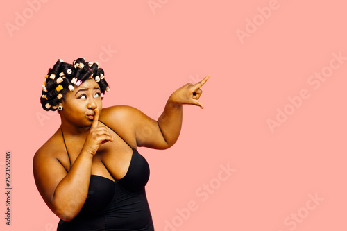 Фотография Portrait of a woman with hair curlers pointing up with finger over her mouth,  i