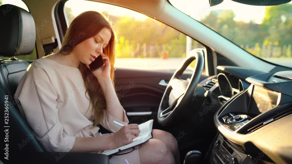 Business woman talking on a smartphone and taking notes in the dairy sitting in the car Business woman talking on a smartphone and taking notes in the dairy sitting in the car