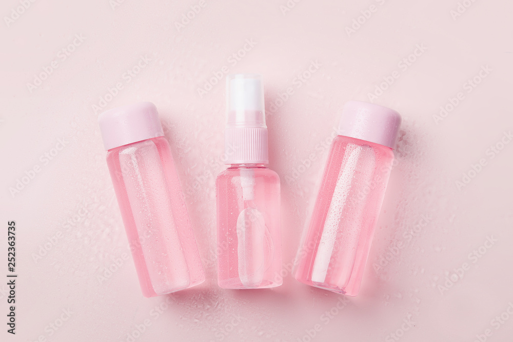 Three bottles of tonic or lotion sprinkled with water on pink or powder background. Freshness and body care. Female cosmetics. Micellar water. Travel set of face care cosmetic Three bottles of tonic or lotion sprinkled with water on pink or powder background. Freshness and body care. Female cosmetics. Micellar water. Travel set of face care cosmetic
