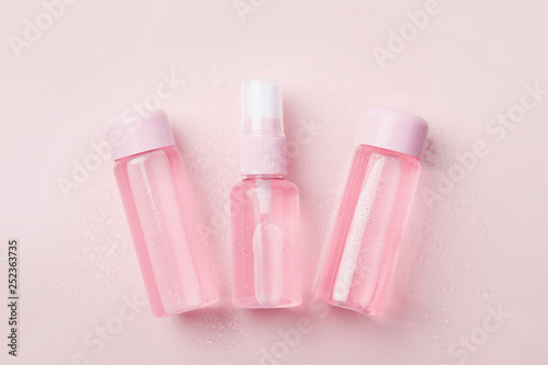 Three bottles of tonic or lotion sprinkled with water on pink or powder background. Freshness and body care. Female cosmetics. Micellar water. Travel set of face care cosmetic