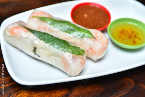 Traditional Vietnamese cuisine dish - fresh spring rolls wrapped in transparent rice paper with prawns, vermicelli, mint and carrots inside served with spicy sauces 