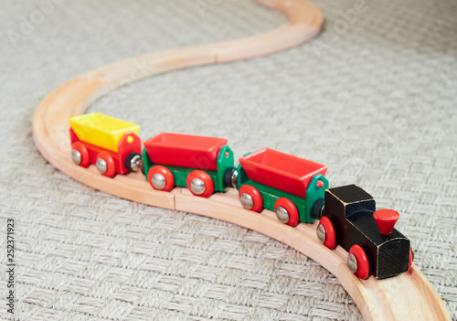 Wooden toy train running on miniature railroad. The black engine pulling colorful cars on the floor. Educational toys for children in preschool and kindergarten.
