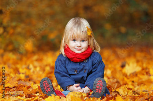 Little autumn funny girl sitting in autumn park. Selective focus, copy space.