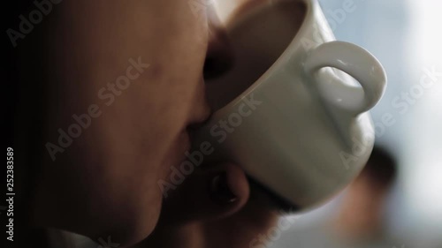 Young beautiful girl in a hat with a cup of coffee in hand and drinking it.