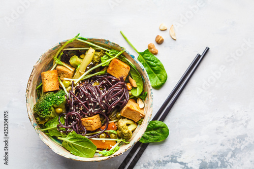 Vegan black rice noodles with tofu and vegetables, white background.
