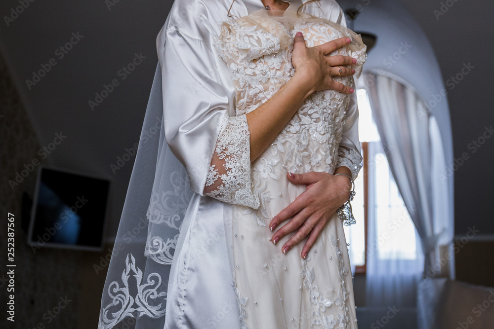bride in bathrobe holding wedding dress in hands