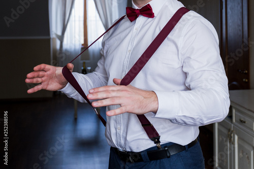 the groom holds his hands suspenders in a suit